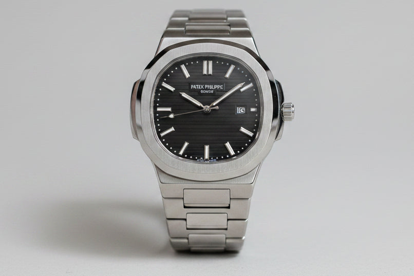 A silver stainless steel wristwatch with a black dial and date window, presented inside an open black gift box with white cushioning.